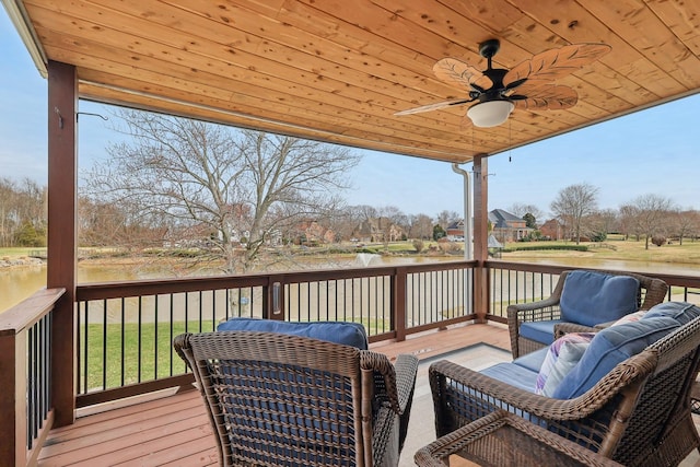 wooden terrace featuring a ceiling fan, a water view, and a lawn