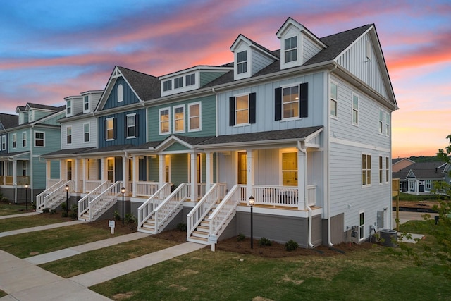 multi unit property featuring covered porch, board and batten siding, a front yard, cooling unit, and stairs