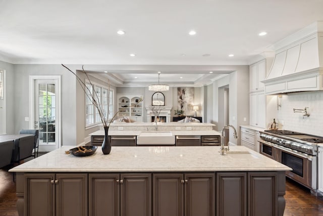 kitchen featuring a sink, white cabinets, a large island, double oven range, and custom range hood