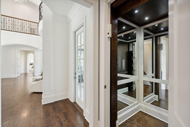 interior space with dark wood-type flooring, arched walkways, crown molding, and baseboards