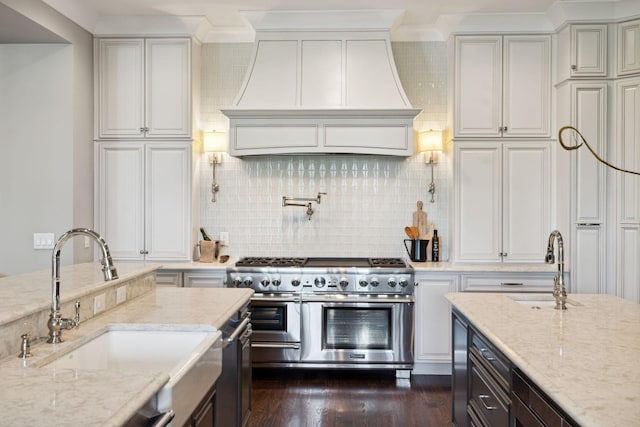 kitchen featuring a sink, double oven range, backsplash, custom exhaust hood, and light stone countertops