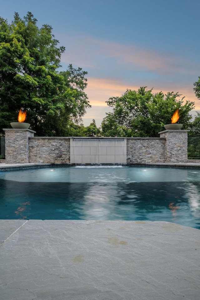 pool at dusk with fence and an outdoor pool