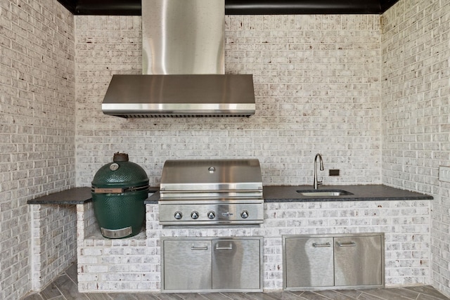 kitchen featuring brick wall, wall chimney range hood, dark countertops, and a sink