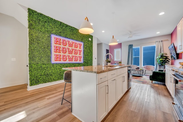 kitchen featuring an island with sink, an accent wall, hanging light fixtures, white cabinetry, and a sink