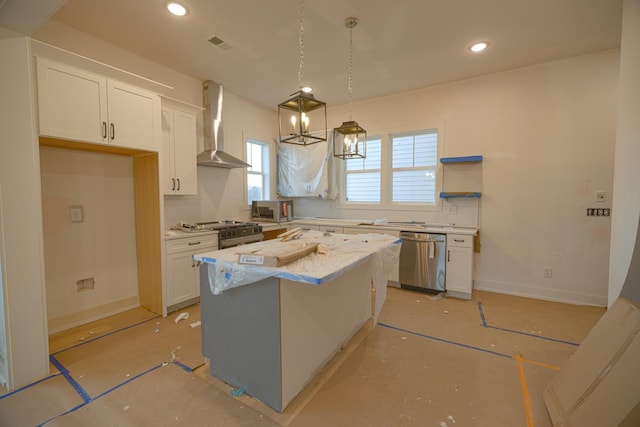 kitchen featuring wall chimney exhaust hood, a center island, stainless steel appliances, white cabinetry, and pendant lighting