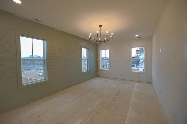 spare room featuring wooden walls, visible vents, and an inviting chandelier