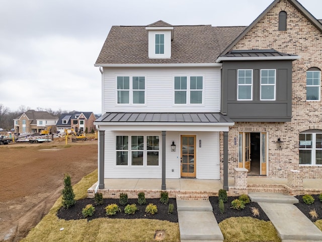 view of front facade featuring a standing seam roof, a shingled roof, a porch, and brick siding