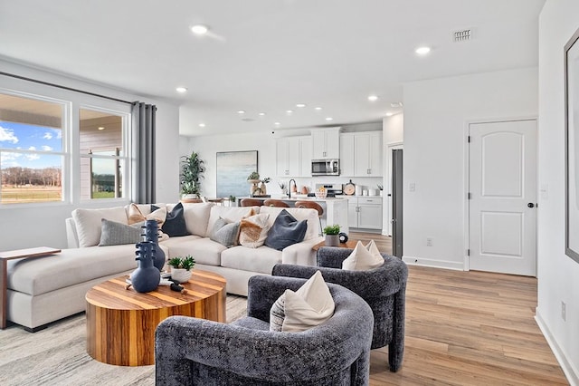 living room featuring baseboards, light wood-style flooring, visible vents, and recessed lighting