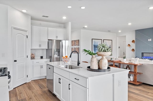 kitchen featuring a sink, white cabinets, open floor plan, appliances with stainless steel finishes, and a center island with sink