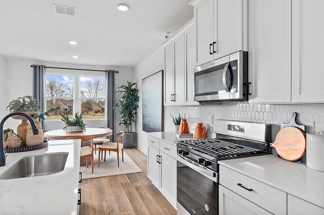 kitchen with light stone counters, stainless steel appliances, visible vents, white cabinets, and decorative backsplash