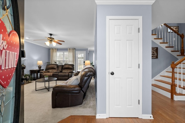 living area with crown molding, stairway, a ceiling fan, light wood-type flooring, and baseboards