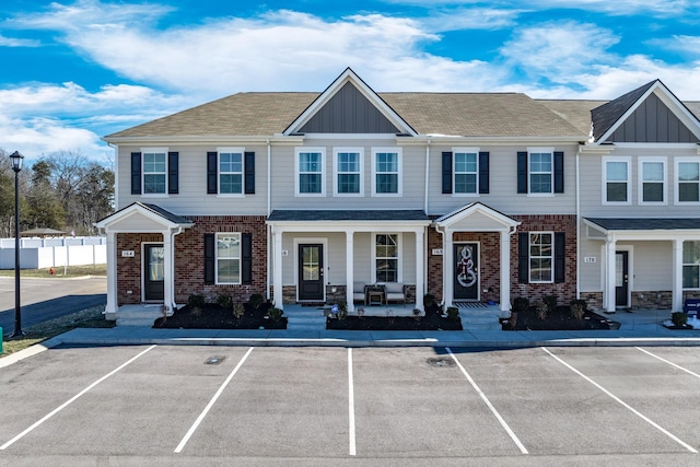 townhome / multi-family property with covered porch, uncovered parking, board and batten siding, and brick siding