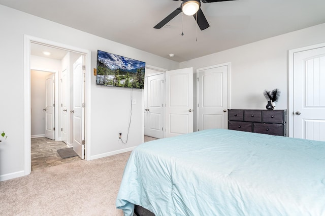 bedroom featuring light carpet, ceiling fan, baseboards, and ensuite bathroom