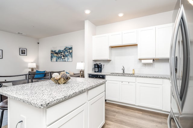 kitchen with freestanding refrigerator, white cabinets, a sink, and light stone countertops