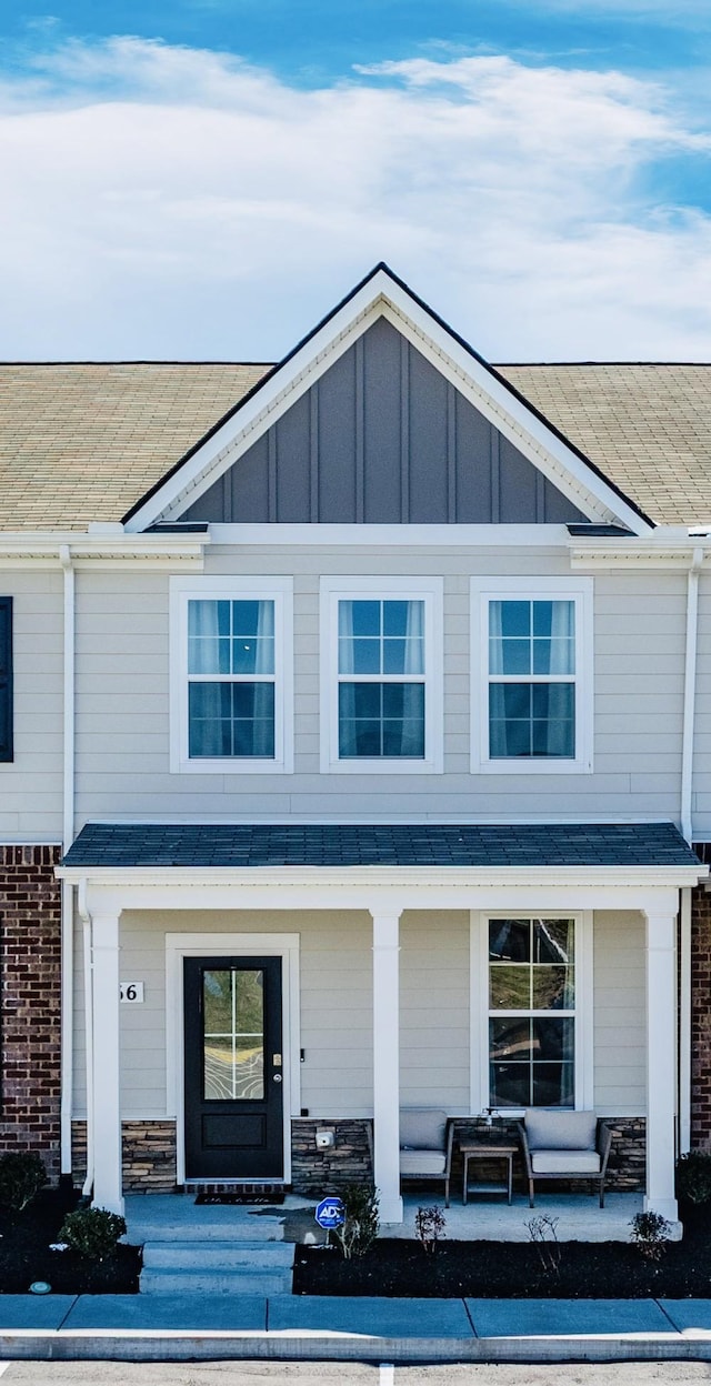 view of exterior entry with board and batten siding, covered porch, and roof with shingles