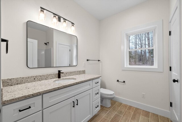 full bath featuring a shower, toilet, wood tiled floor, vanity, and baseboards