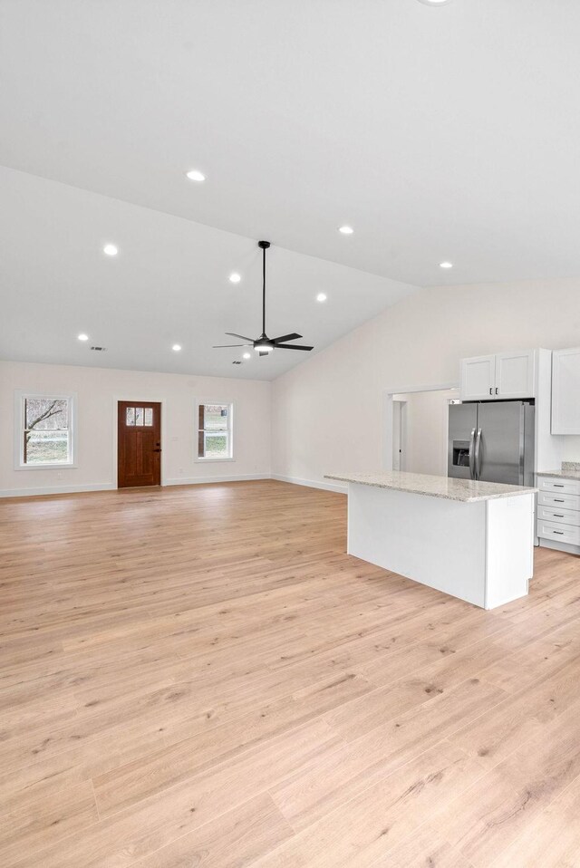 kitchen with stainless steel fridge, white cabinets, open floor plan, light wood-type flooring, and recessed lighting