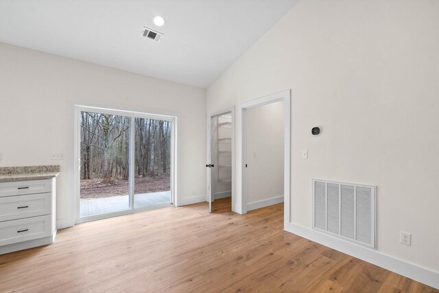 unfurnished room with light wood finished floors, baseboards, visible vents, and vaulted ceiling