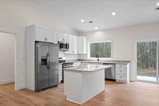 kitchen with a center island, appliances with stainless steel finishes, white cabinetry, light stone countertops, and light wood-type flooring