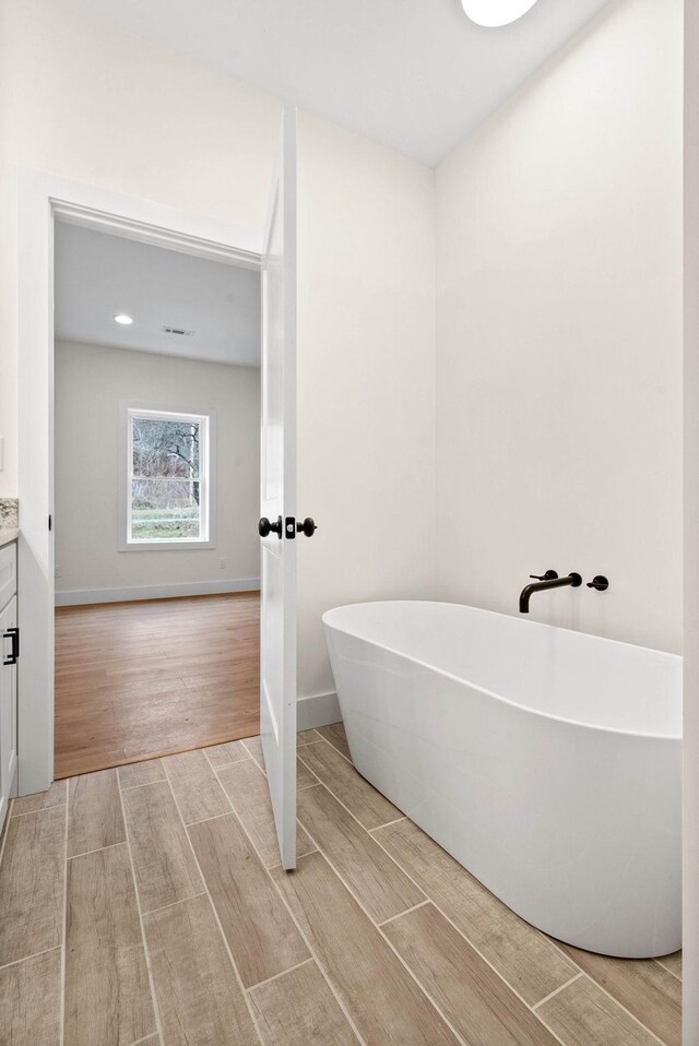 full bathroom featuring a freestanding tub, wood tiled floor, baseboards, and vanity