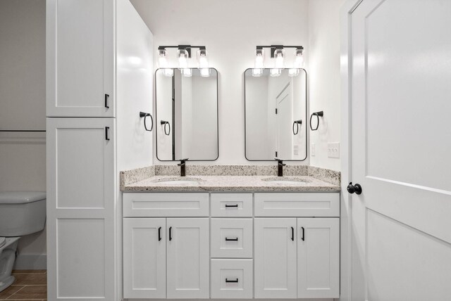 bathroom featuring toilet, double vanity, a sink, and tile patterned floors