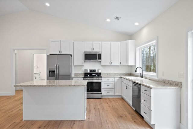 kitchen featuring a kitchen island, light stone counters, stainless steel appliances, white cabinetry, and a sink