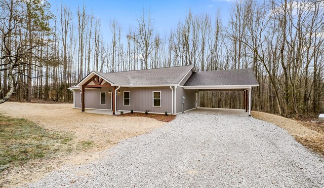 ranch-style home featuring gravel driveway, covered porch, a carport, and roof with shingles