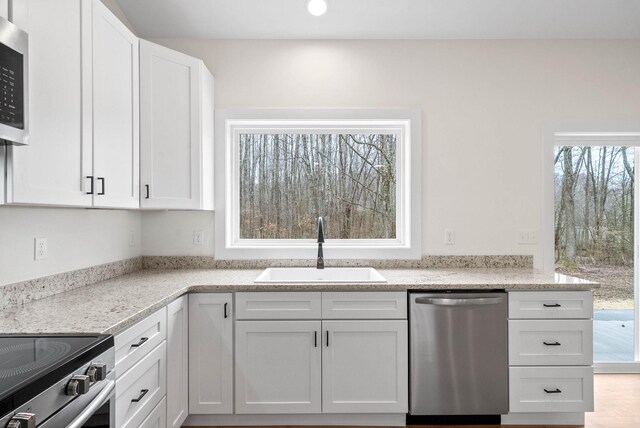 kitchen featuring appliances with stainless steel finishes, a sink, light stone countertops, and white cabinets