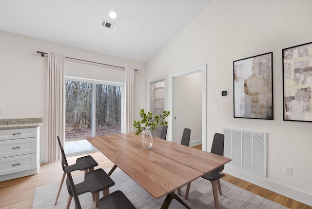 dining area featuring light wood-type flooring, visible vents, and vaulted ceiling