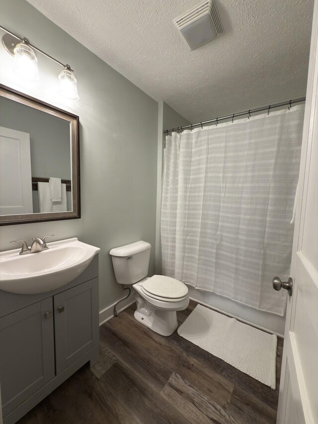 full bath featuring visible vents, toilet, vanity, a textured ceiling, and wood finished floors