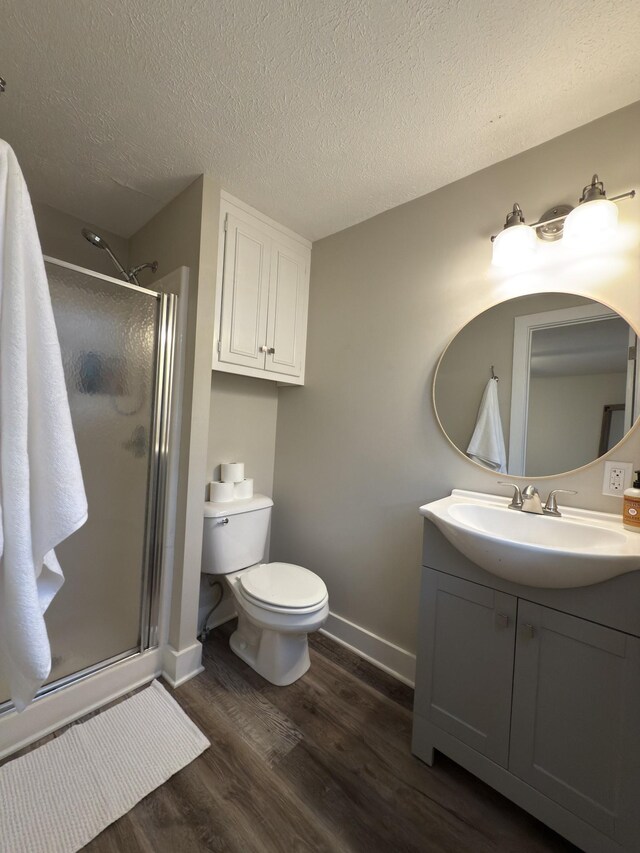 full bathroom with a textured ceiling, wood finished floors, vanity, baseboards, and a shower stall