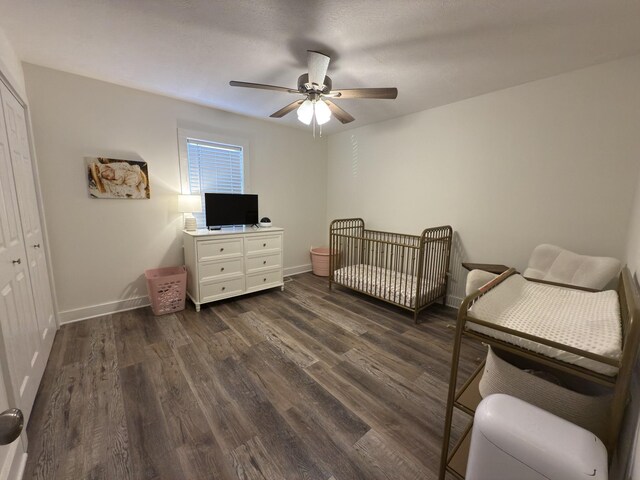 bedroom with a nursery area, ceiling fan, baseboards, and dark wood finished floors