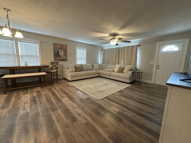 living room with dark wood-type flooring, a textured ceiling, baseboards, and ceiling fan with notable chandelier