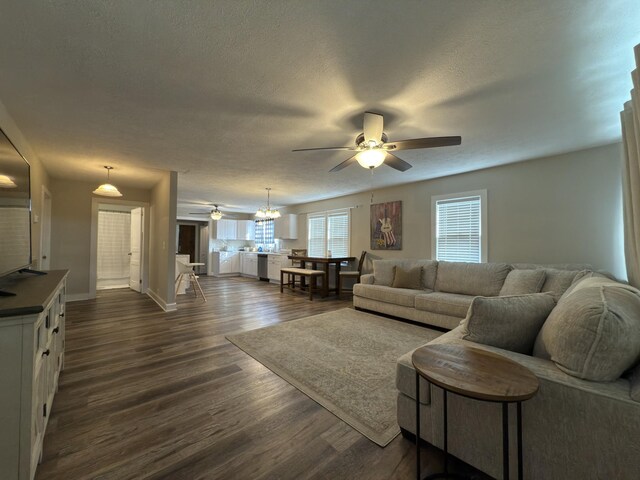 living area featuring a textured ceiling, baseboards, dark wood-type flooring, and ceiling fan with notable chandelier