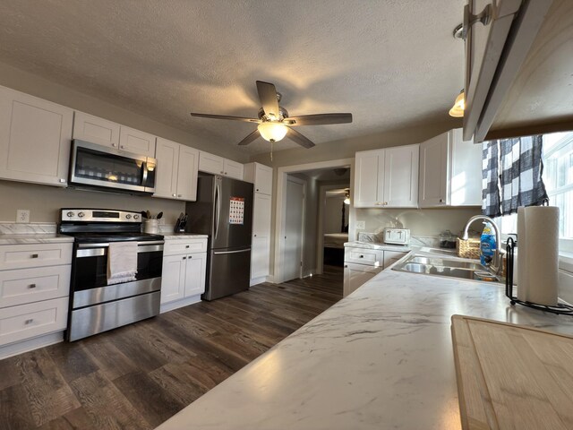 kitchen featuring dark wood-type flooring, hanging light fixtures, stainless steel appliances, white cabinetry, and a sink