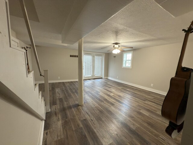 below grade area with dark wood-style flooring, stairway, a ceiling fan, a textured ceiling, and baseboards