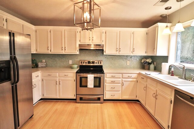 kitchen with appliances with stainless steel finishes, light countertops, under cabinet range hood, pendant lighting, and a sink