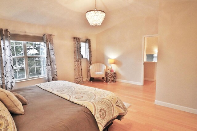 bedroom featuring a chandelier, vaulted ceiling, baseboards, and light wood-style floors