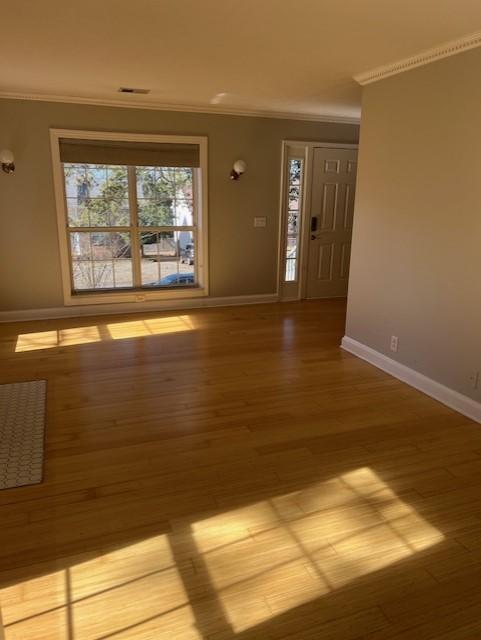 entrance foyer featuring light wood finished floors, ornamental molding, visible vents, and baseboards