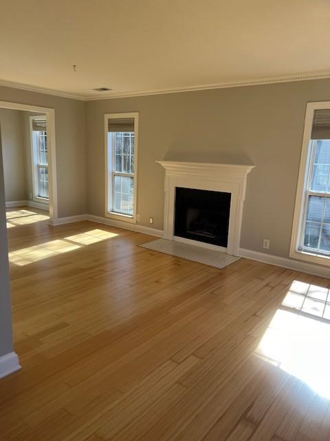 unfurnished living room featuring ornamental molding, a fireplace with flush hearth, light wood-style flooring, and baseboards