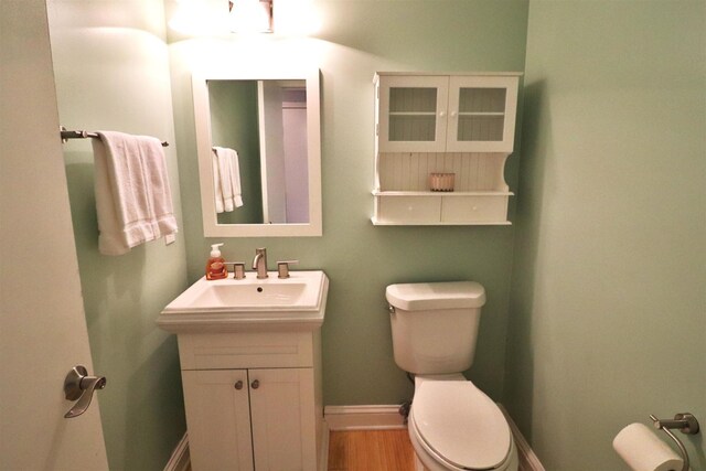 half bathroom featuring toilet, baseboards, wood finished floors, and vanity