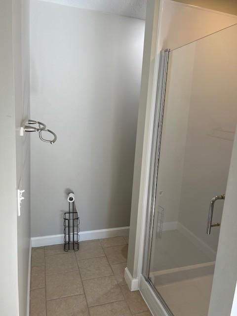 full bath with tile patterned flooring, a shower stall, and baseboards