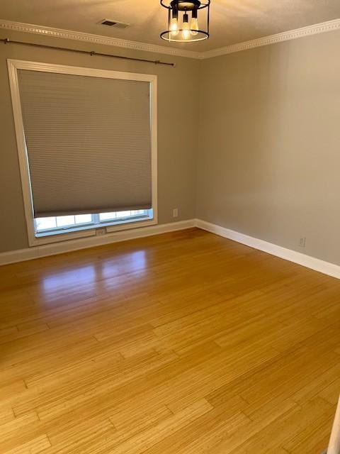 empty room with crown molding, baseboards, visible vents, and light wood-style floors