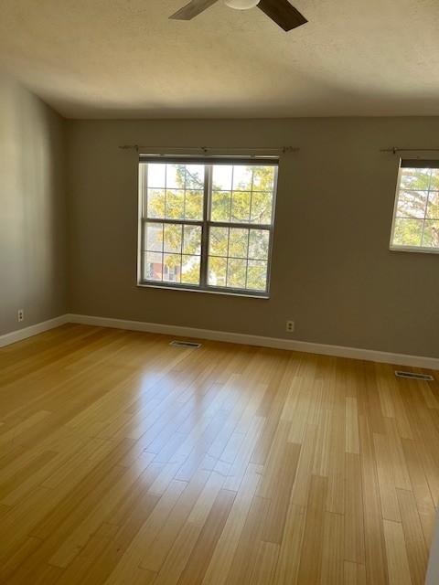 unfurnished room with baseboards, ceiling fan, visible vents, and light wood-style floors