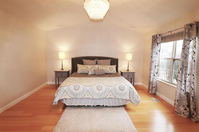 bedroom with a chandelier, wood finished floors, visible vents, and baseboards