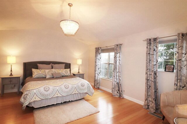 bedroom featuring light wood-type flooring, multiple windows, baseboards, and a notable chandelier