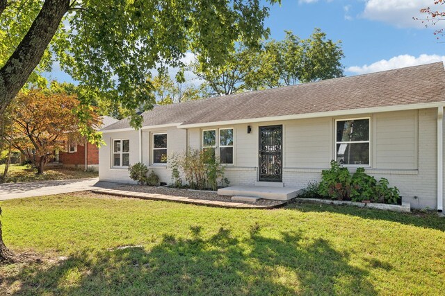 single story home with a shingled roof, a front yard, and brick siding