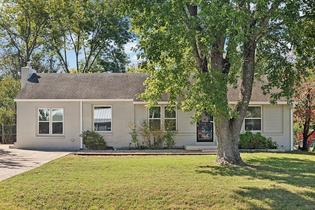 ranch-style home with roof with shingles, brick siding, a chimney, and a front yard