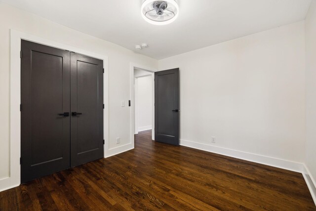 unfurnished bedroom featuring dark wood-type flooring, a closet, and baseboards