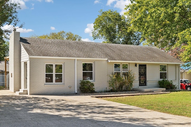 ranch-style home featuring brick siding, driveway, roof with shingles, a chimney, and a front yard